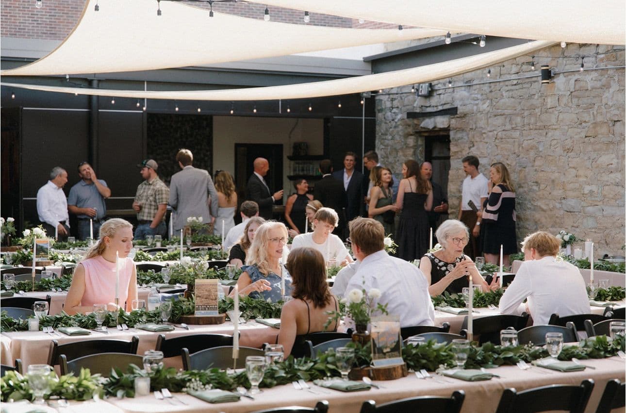 Long tables with greenery runners set for dinner in the courtyard, under shade sails and string lights