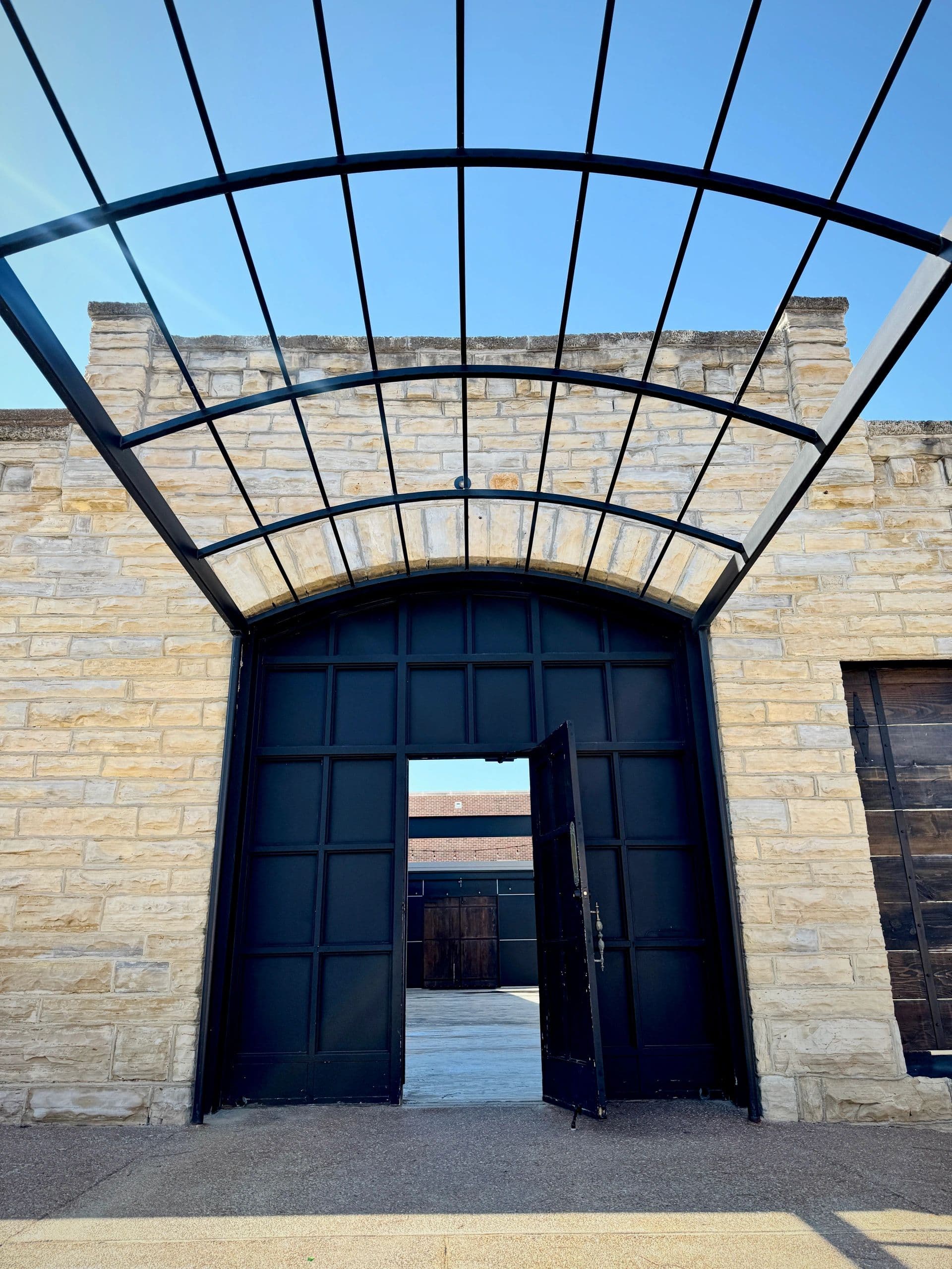 The arched steel canopy over the tall black courtyard gate at Venue 324, one door standing open to the courtyard beyond