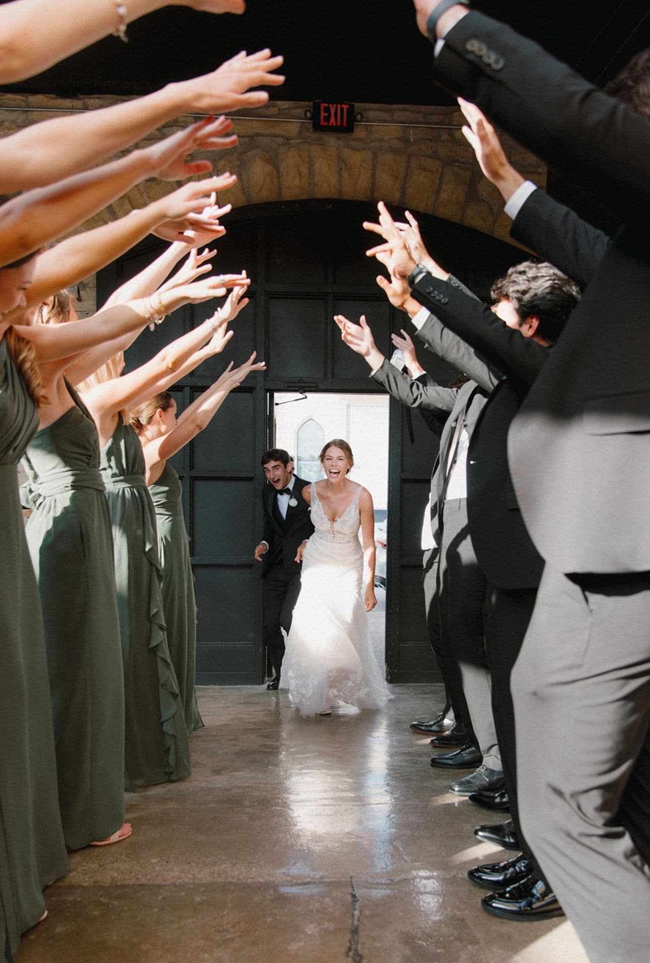 A couple entering through the arched stone doorway as their wedding party cheers