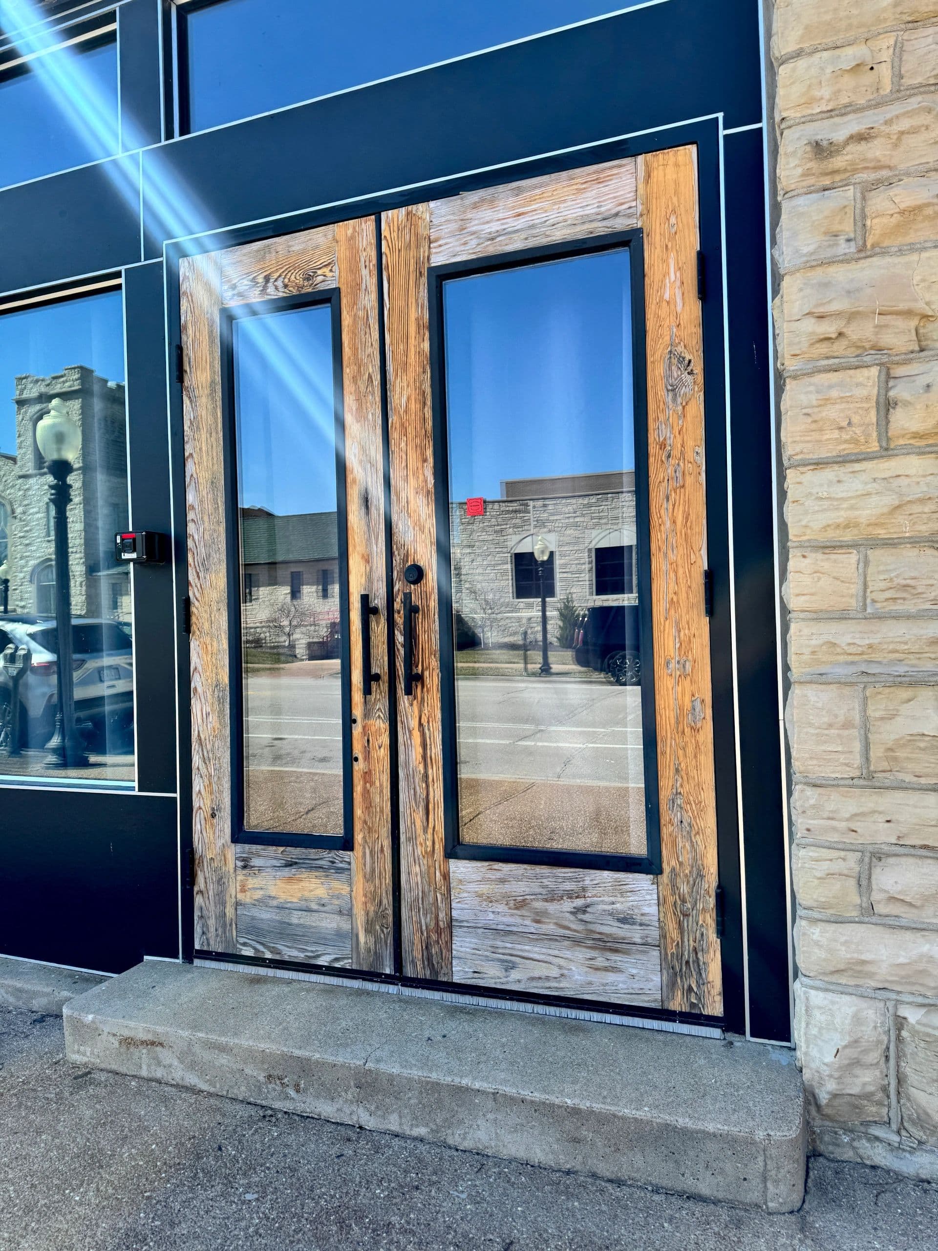 The reclaimed-timber entry doors at Venue 324 in their black steel frame, the limestone wall beside them and the street reflected in the glass
