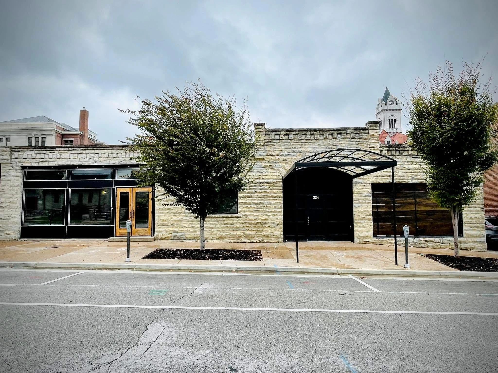 The limestone facade of Venue 324 at 324 East Capitol Avenue, with its black arched entrance canopy and a church steeple rising behind